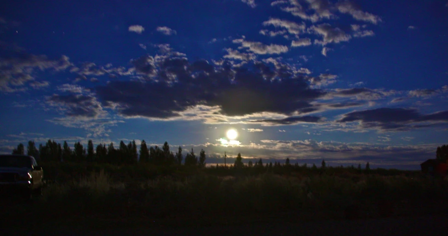 a full moon is lit in the sky with a cloud trail