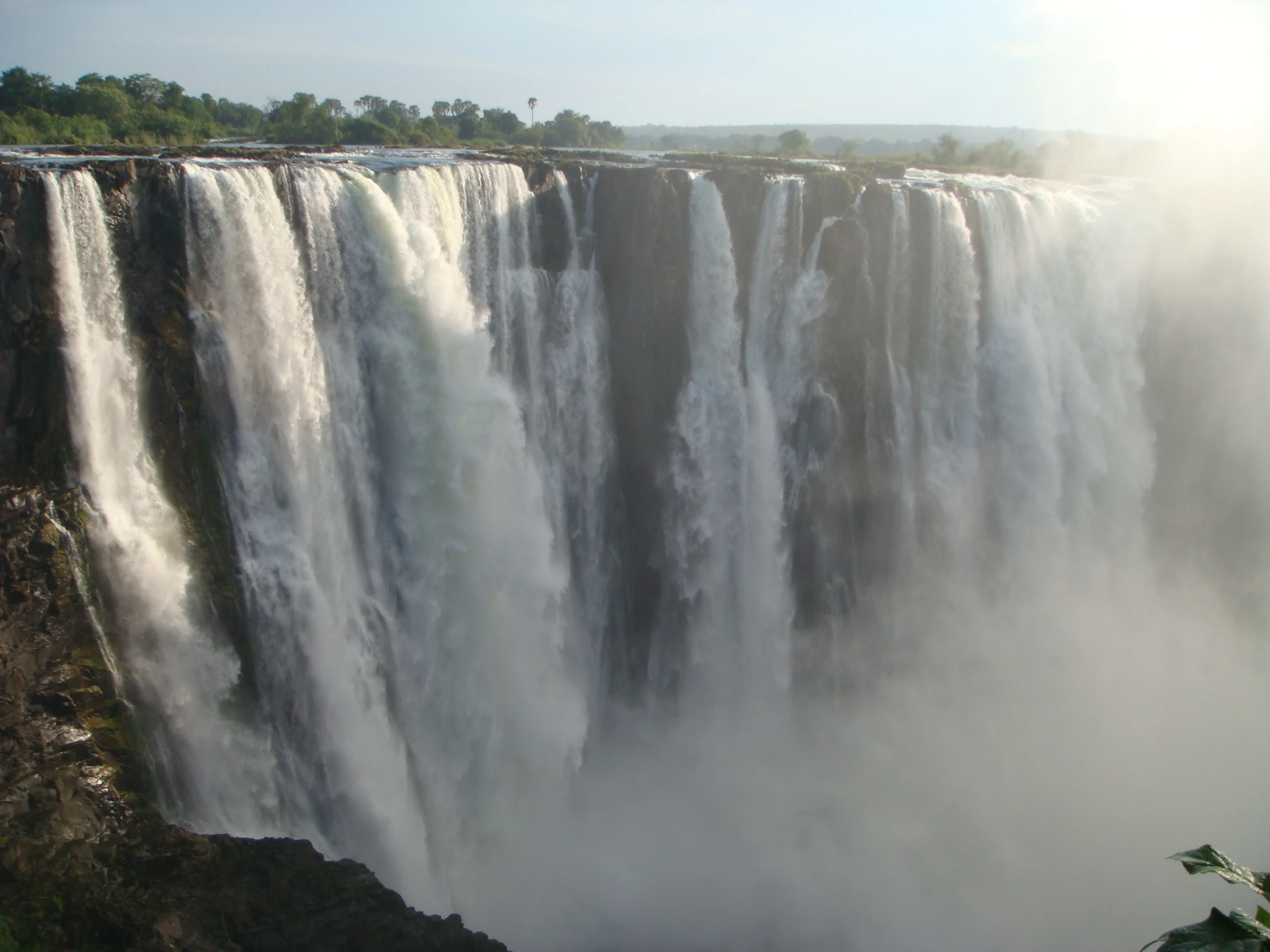 large waterfall on the edge of a river and surrounded by trees