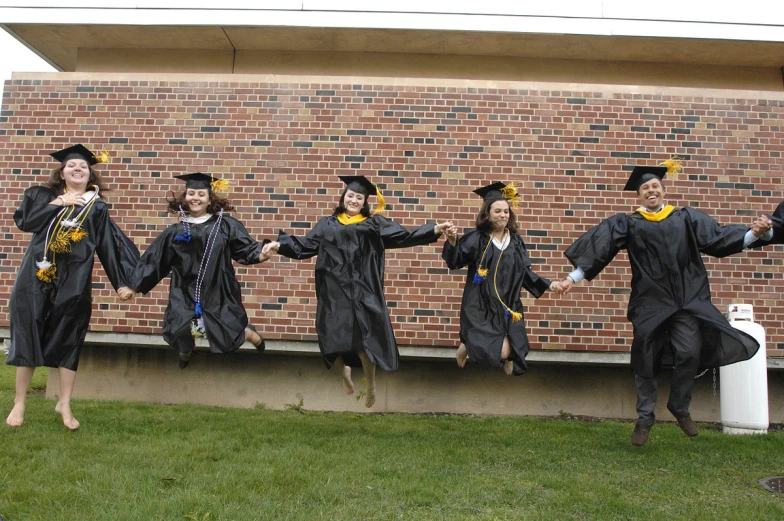 group of graduates jump up in the air in graduation gowns