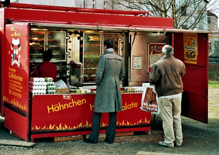 two men are standing at a red food cart