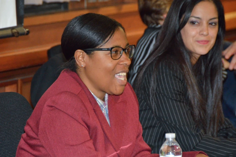 a woman laughing while looking at another woman holding a water bottle