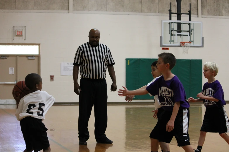 two referees are directing young s on the basketball court