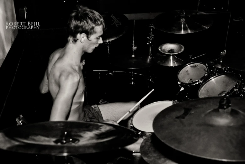 the shirtless young man is playing the drums