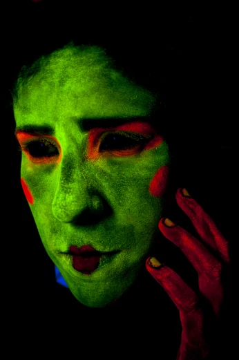 a woman painted in green and red with her hands on the ear