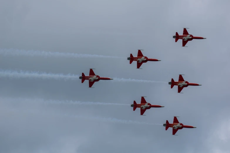 eight red jets are flying in formation on a cloudy day