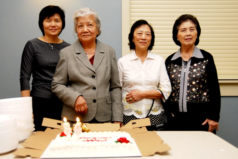 three women standing in front of a birthday cake