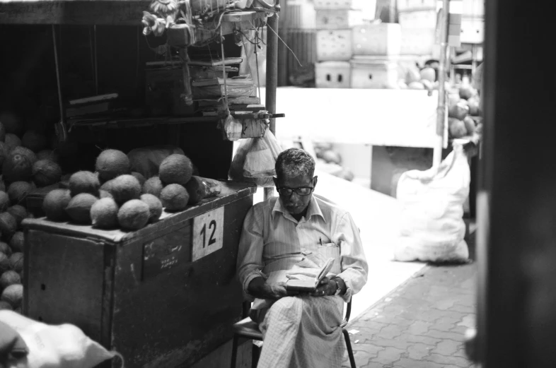 a black and white pograph of a man with a cane in front of a fruit stand