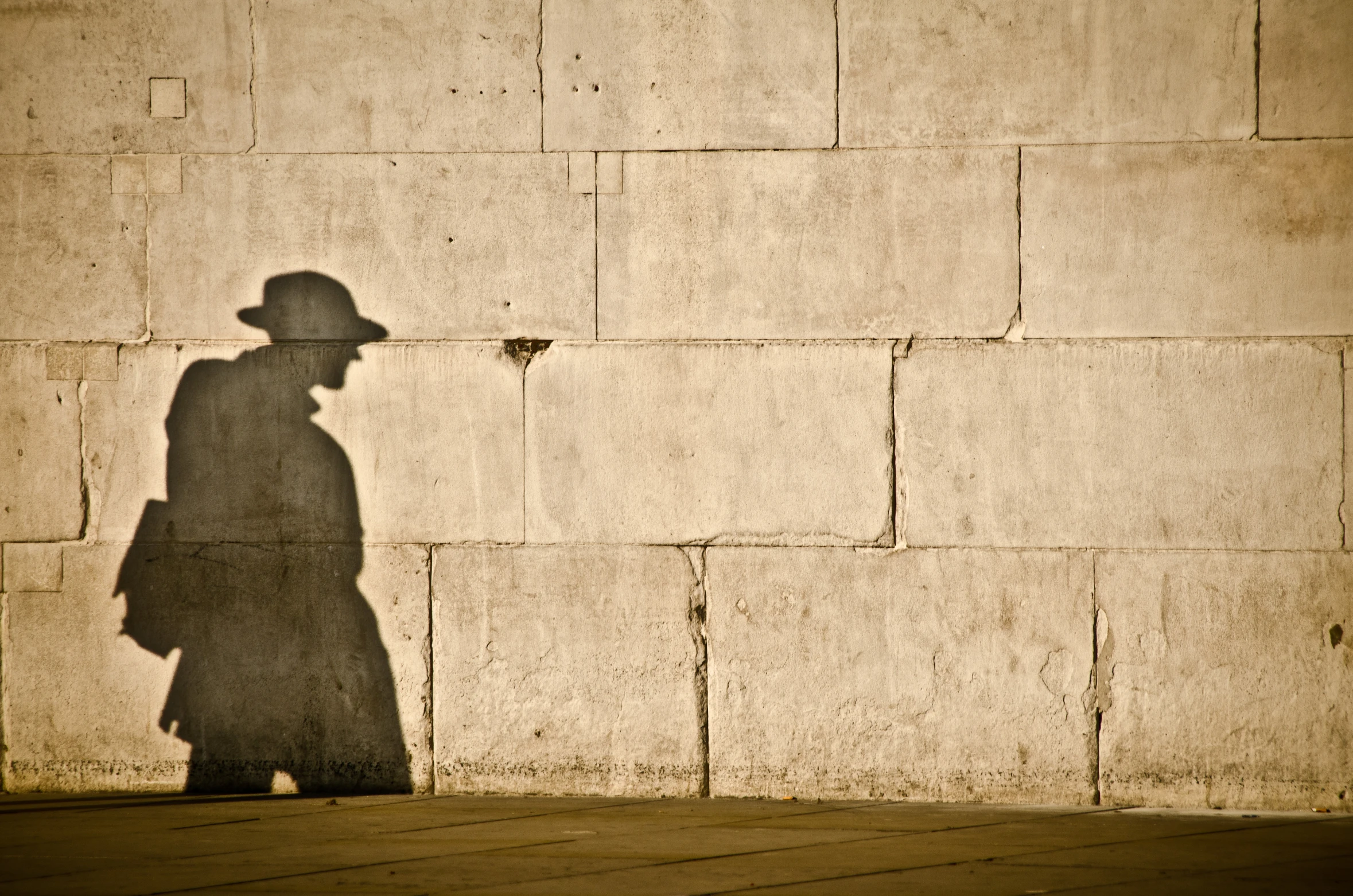 an older person with a hat and a backpack walks past a concrete wall