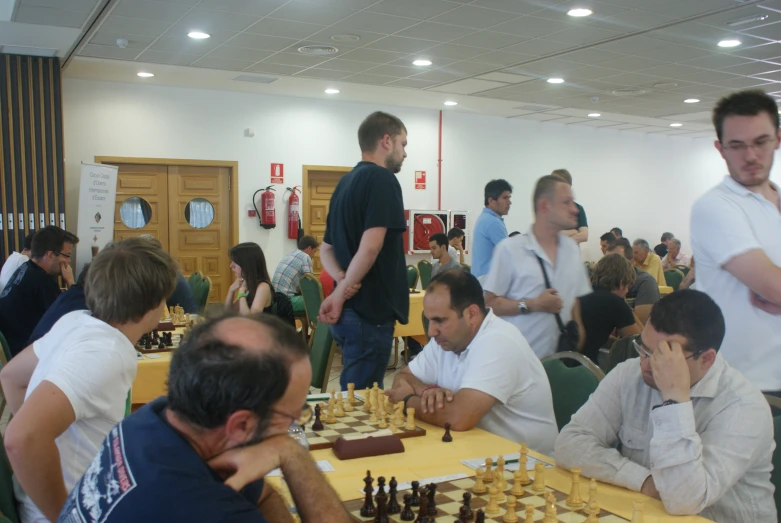 men sit and stand at tables playing chess