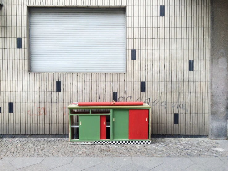a green and red bench sitting next to a white building