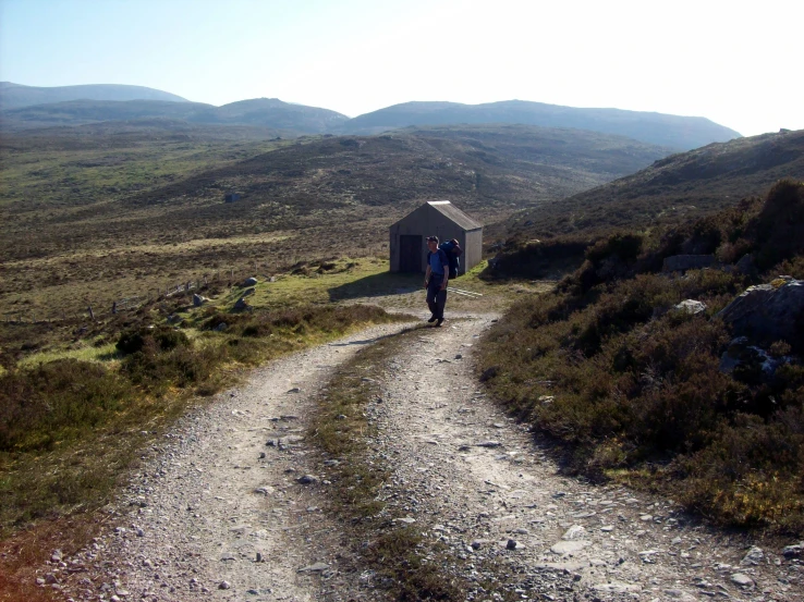 an outhouse sits on a gravel path through the grass and rocks