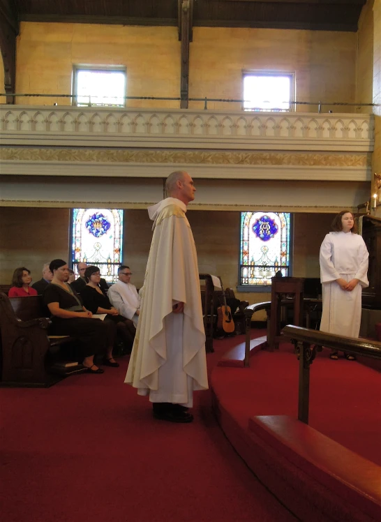 people in chairs at the alter with a priest in white