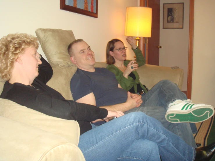 three people on a couch with their feet up, two sitting and one standing