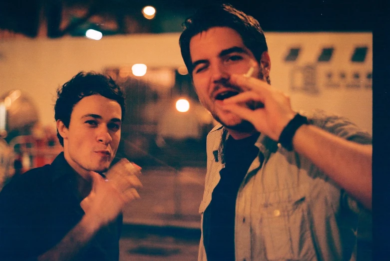 two young men with cigarettes look at the camera