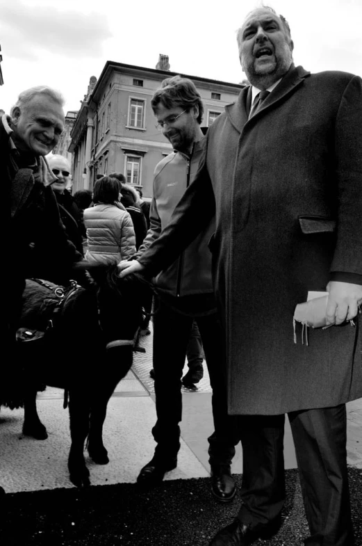 a group of people standing on a sidewalk with one man in a coat