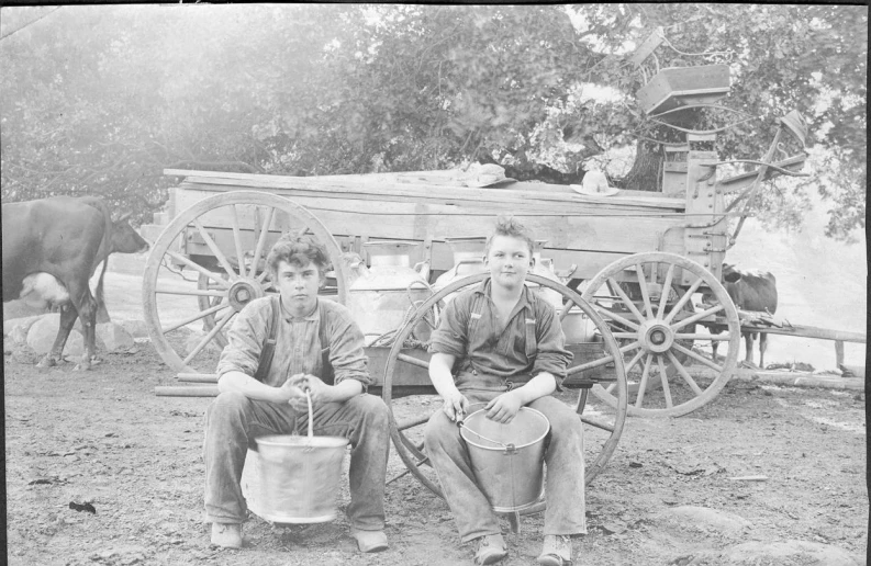 two men sitting on top of a bench near a wagon