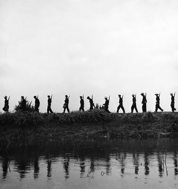 black and white pograph of people walking along side a river