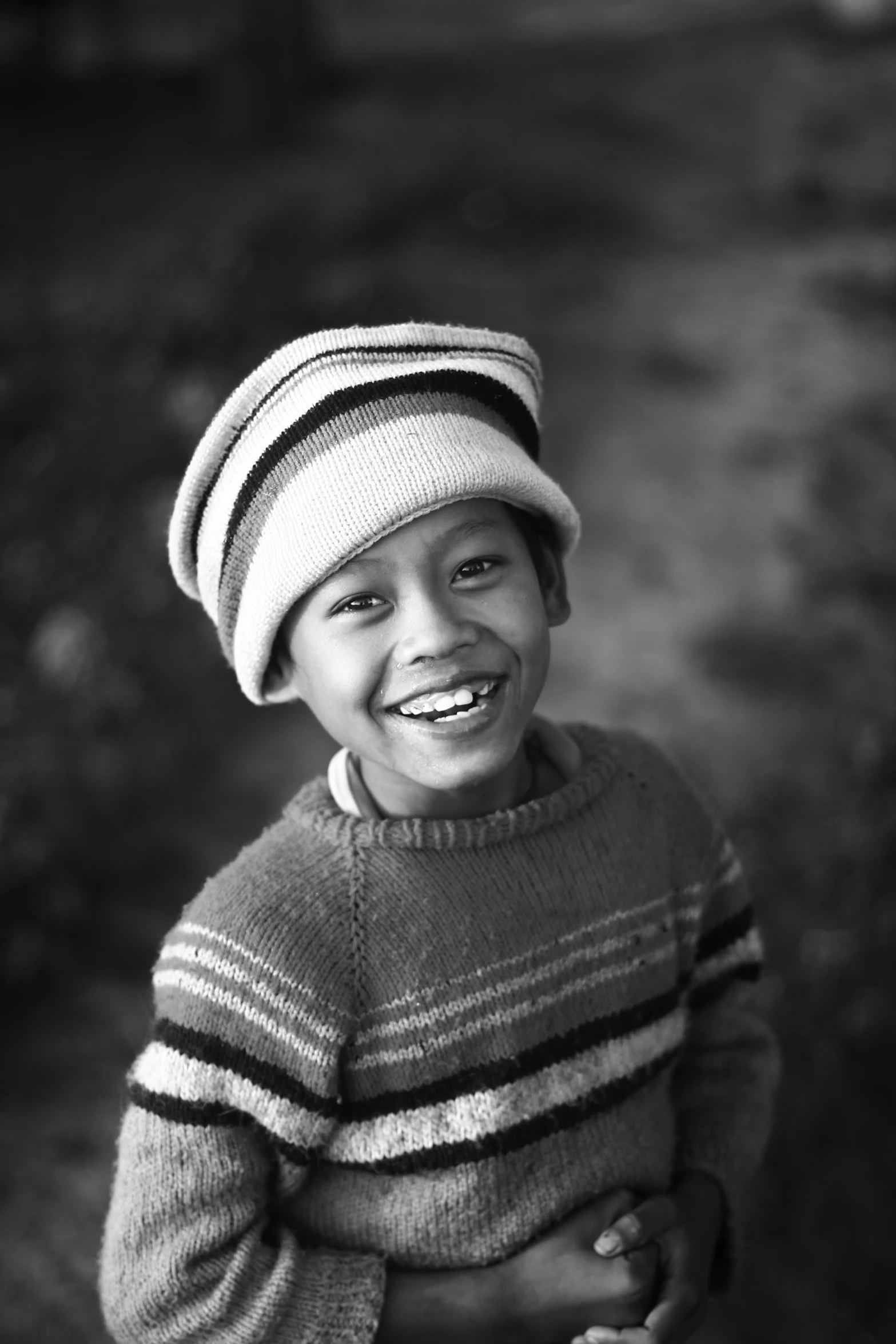a little boy in striped sweater and hat with one hand out