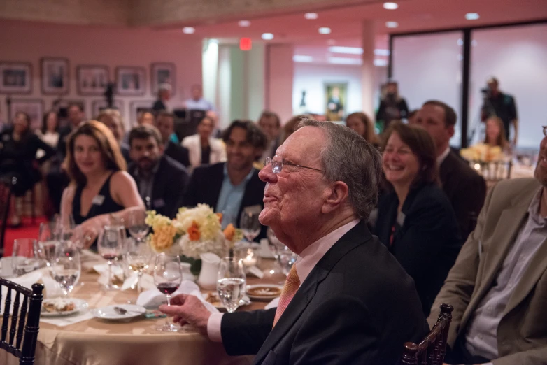 a man at a table smiling while holding a wine glass