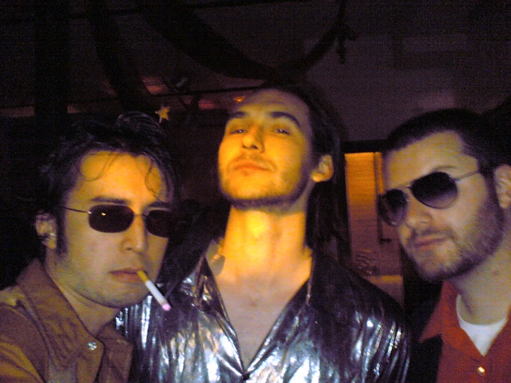 three guys with cigarettes sitting in a bar