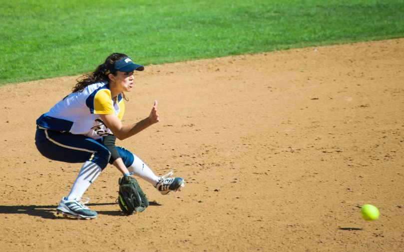 a woman playing baseball kneeling down to catch the ball