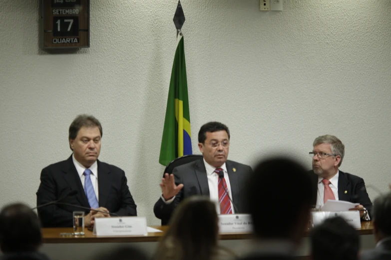 three men in business suits sitting in front of flags