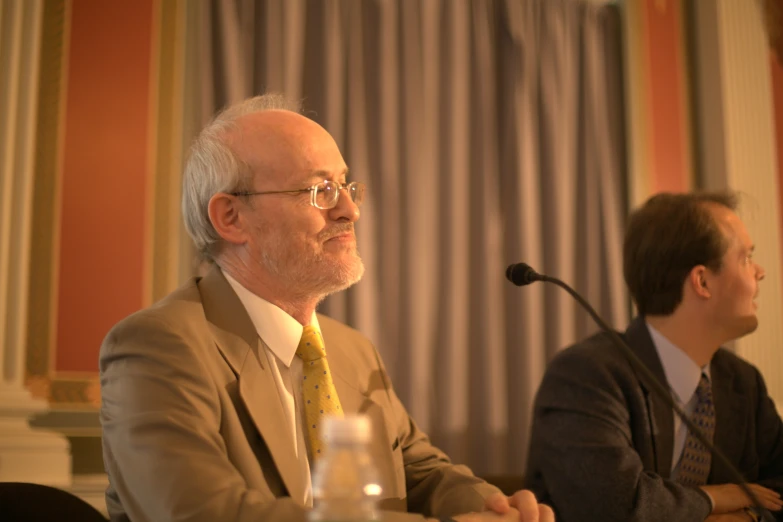 two men are seated at a table with microphone in the background