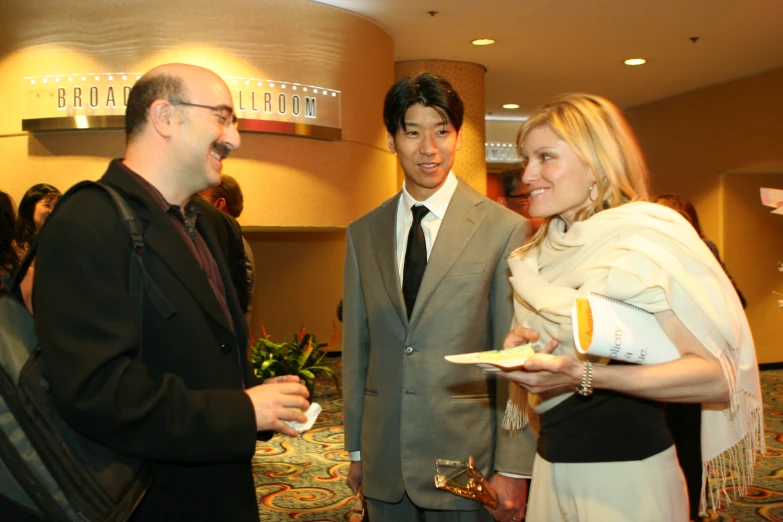 man in black suit standing with other people and smiling