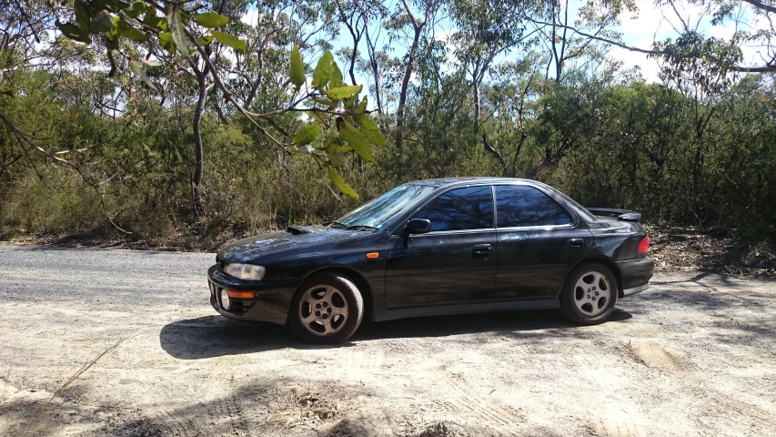 a black car parked in the middle of a dirt road