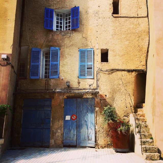 a tan building with blue shutters and potted plants