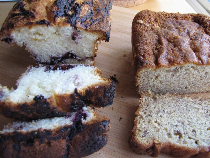 sliced up loafs of blueberry banana bread sitting on top of a wooden  board