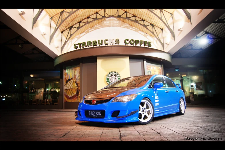 blue car sitting on top of a tile floor in front of a starbucks