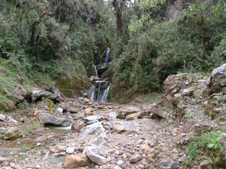 several rocks and a waterfall in the middle of a dirt and green area