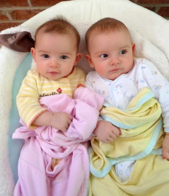 two young babies laying on a blue and yellow blanket