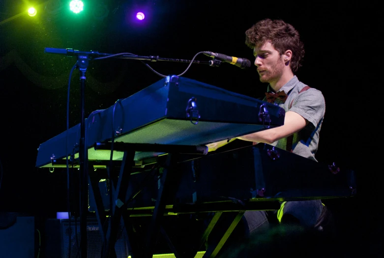 a guy playing a keyboard with lights and microphone behind him