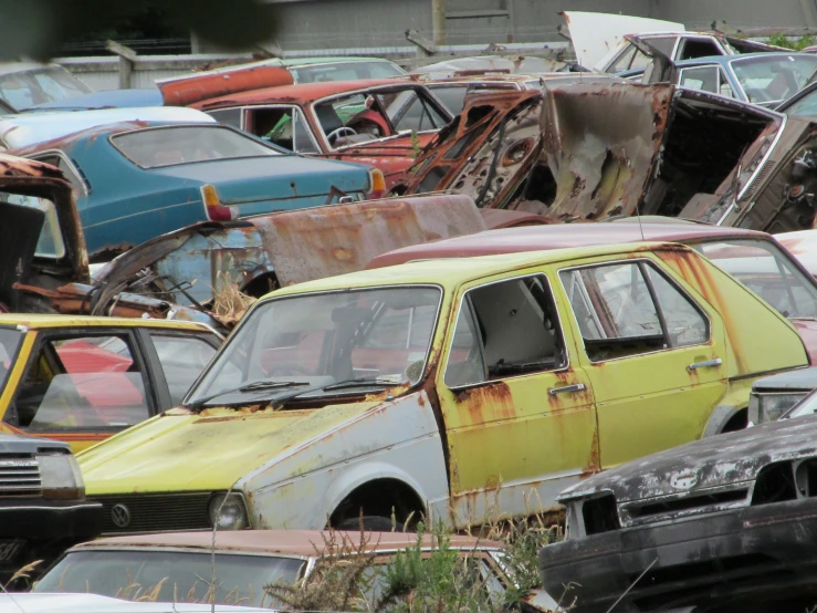 an old yellow car sits in the junkyard