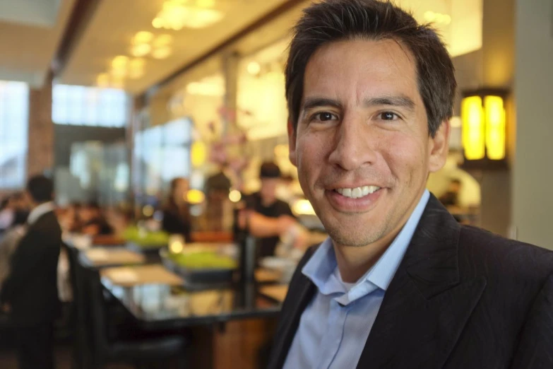 a smiling man in business suit standing next to a large room with many tables and chairs