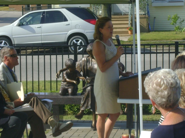 a woman is speaking to people who are seated under an awning