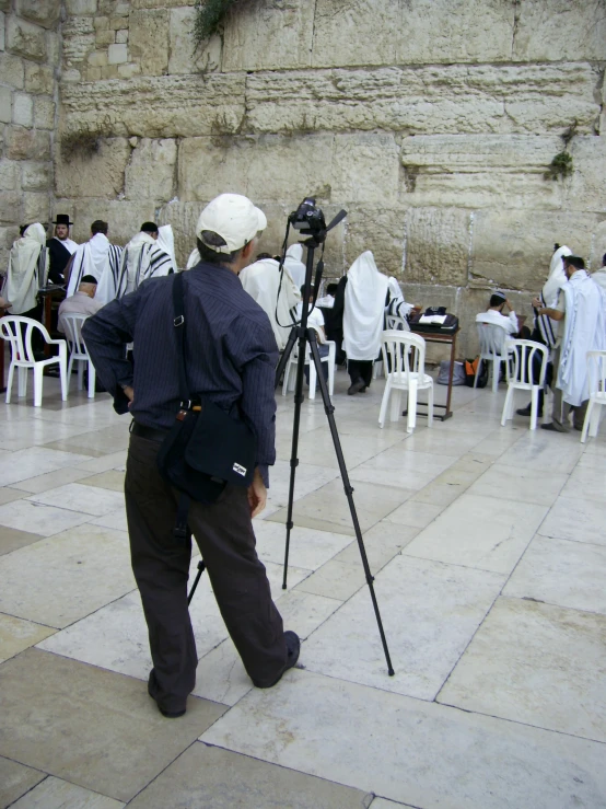 a man in hat standing behind a camera on a tripod