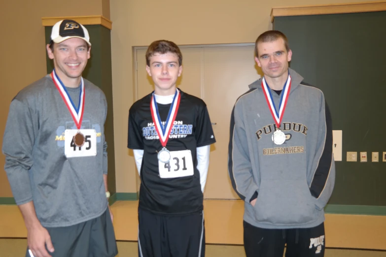 three men standing next to each other holding medals