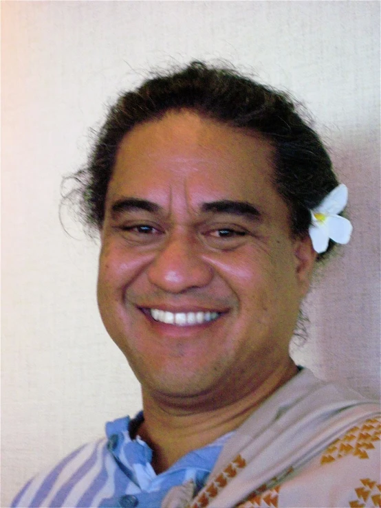 a smiling man wearing a blue shirt and a flower in his hair