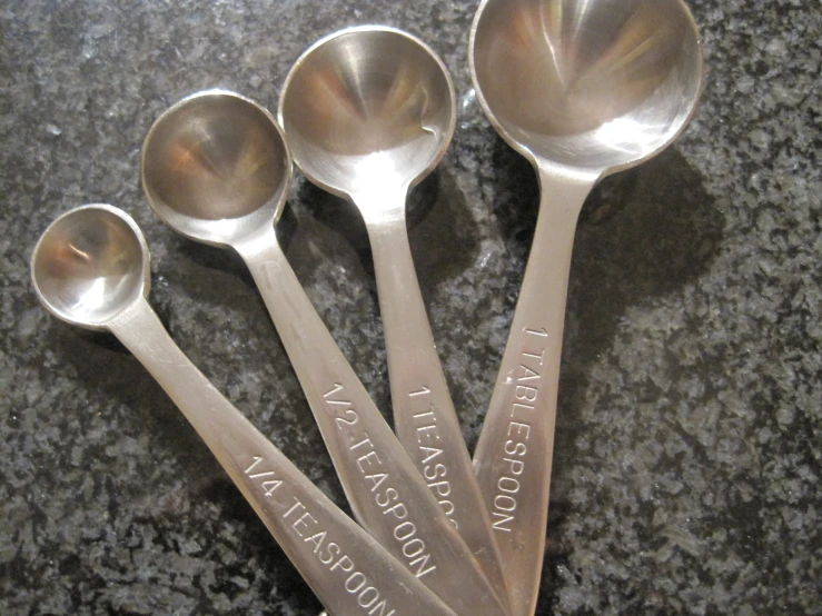 four spoons in different sizes sitting on top of a marble counter