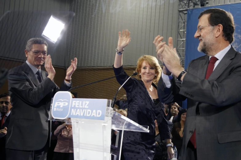 two men and a women stand at podium with their hands raised to the air