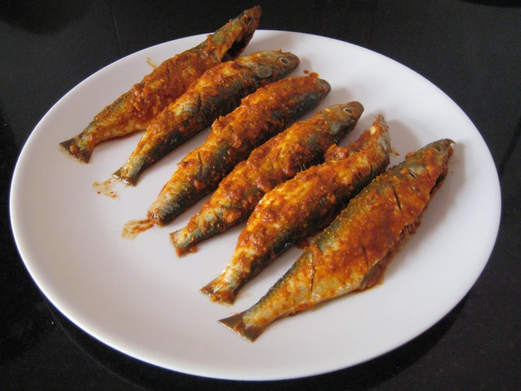 a white plate topped with five fish on top of sauce