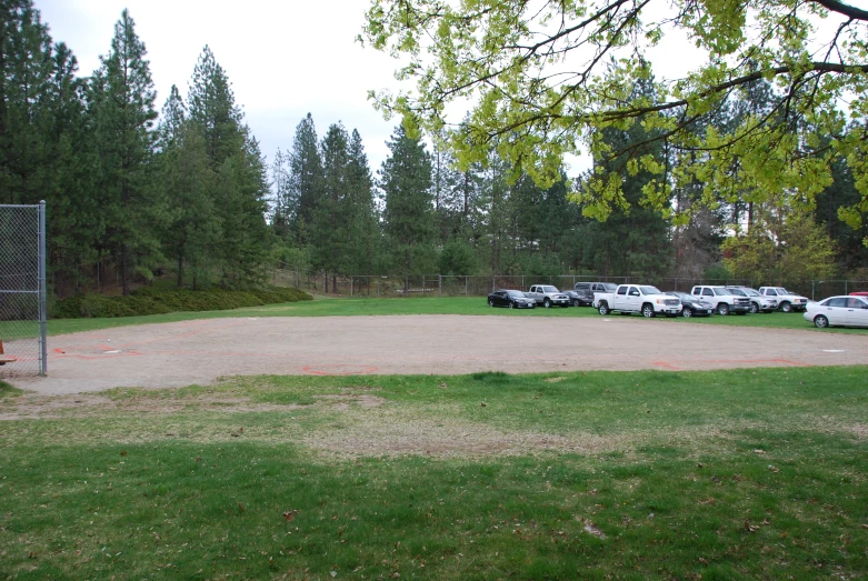 a grassy baseball field surrounded by parked cars