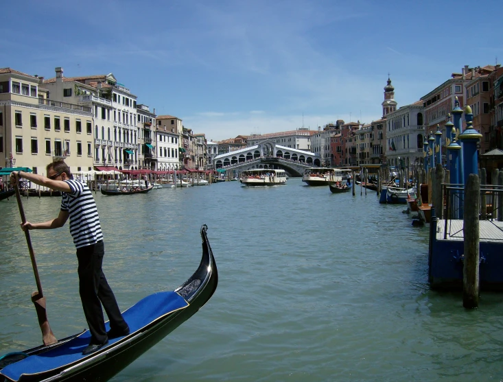 a man in striped shirt paddling a gondola in a narrow body of water