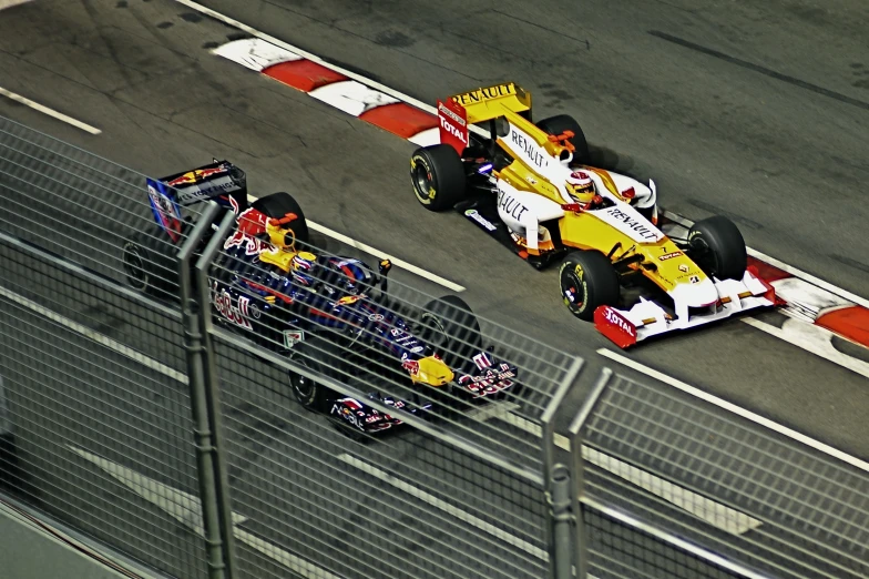 two racing cars drive down the road behind a fence