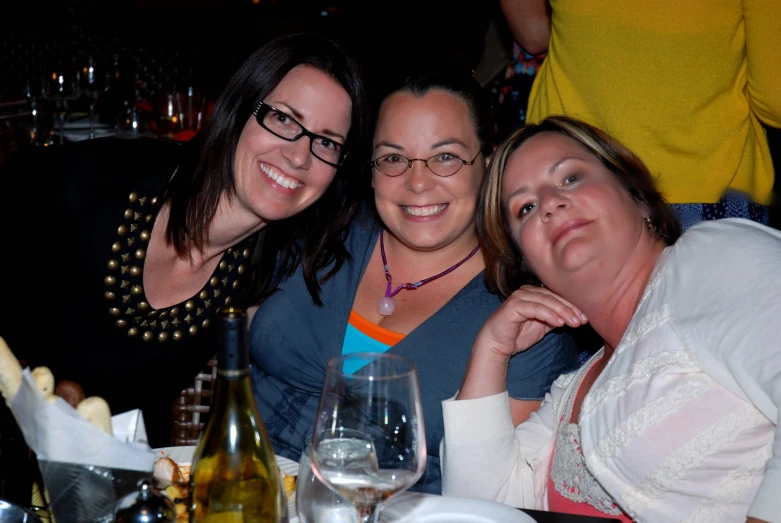 three women posing for the camera in front of several wine glasses