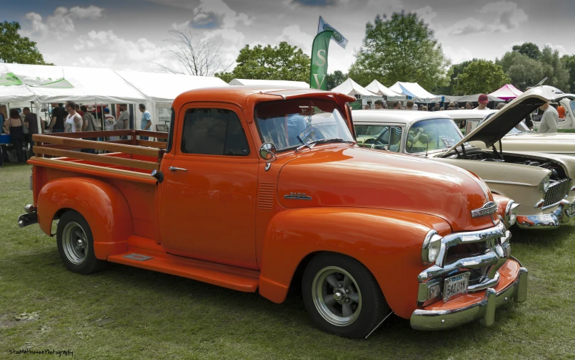 a close - up of the old fashion, rusted orange truck parked near other antique cars