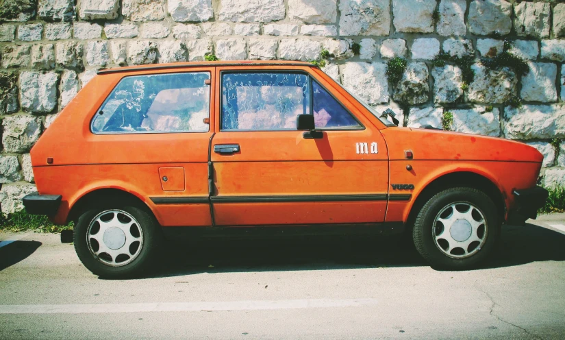 an orange car parked on the street by a wall